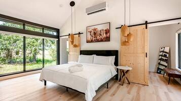 Un dormitorio moderno con una cama grande, una mesita redonda pequeña y vistas al verdor exterior.