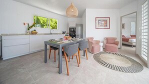 A modern kitchen with white cabinets, a dining area with a table and chairs, and a living room with a pink chair and a round rug. - An Ti Doucè—Villa with a pool, 300 meters from the beach (Sainte-Luce)