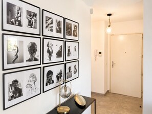 Un corridoio con fotografie in bianco e nero incorniciate alle pareti, un tavolo con una lampada e una porta in fondo.