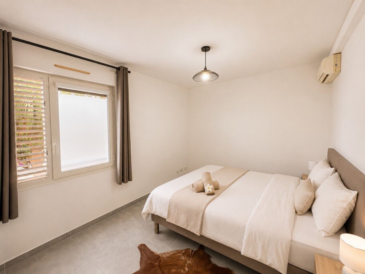 A bedroom with a bed, a window with curtains, a ceiling light, and a rug.