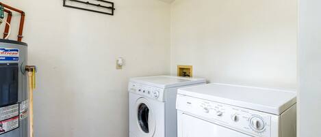 A laundry room with two white washing machines, a heater, and a wooden floor.