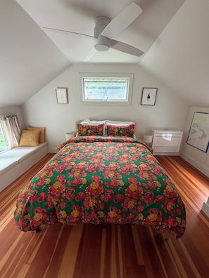 Une chambre à coucher avec un lit, un ventilateur de plafond, une fenêtre et un tableau encadré au mur.