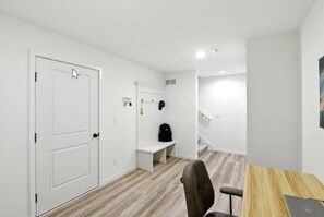 A room with a door, a bench, a desk with a chair, and a laptop.