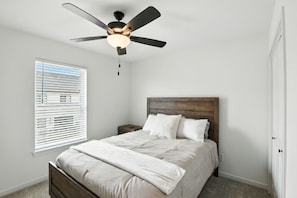 A bedroom with a bed, a nightstand, a ceiling fan, and a window with blinds.