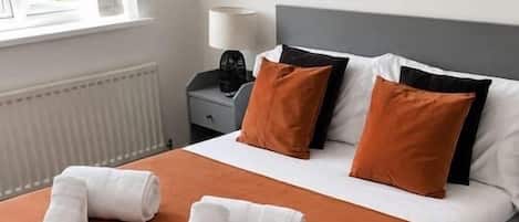 A neatly made bed with white and orange bedding, a gray headboard, and a painting on the wall.