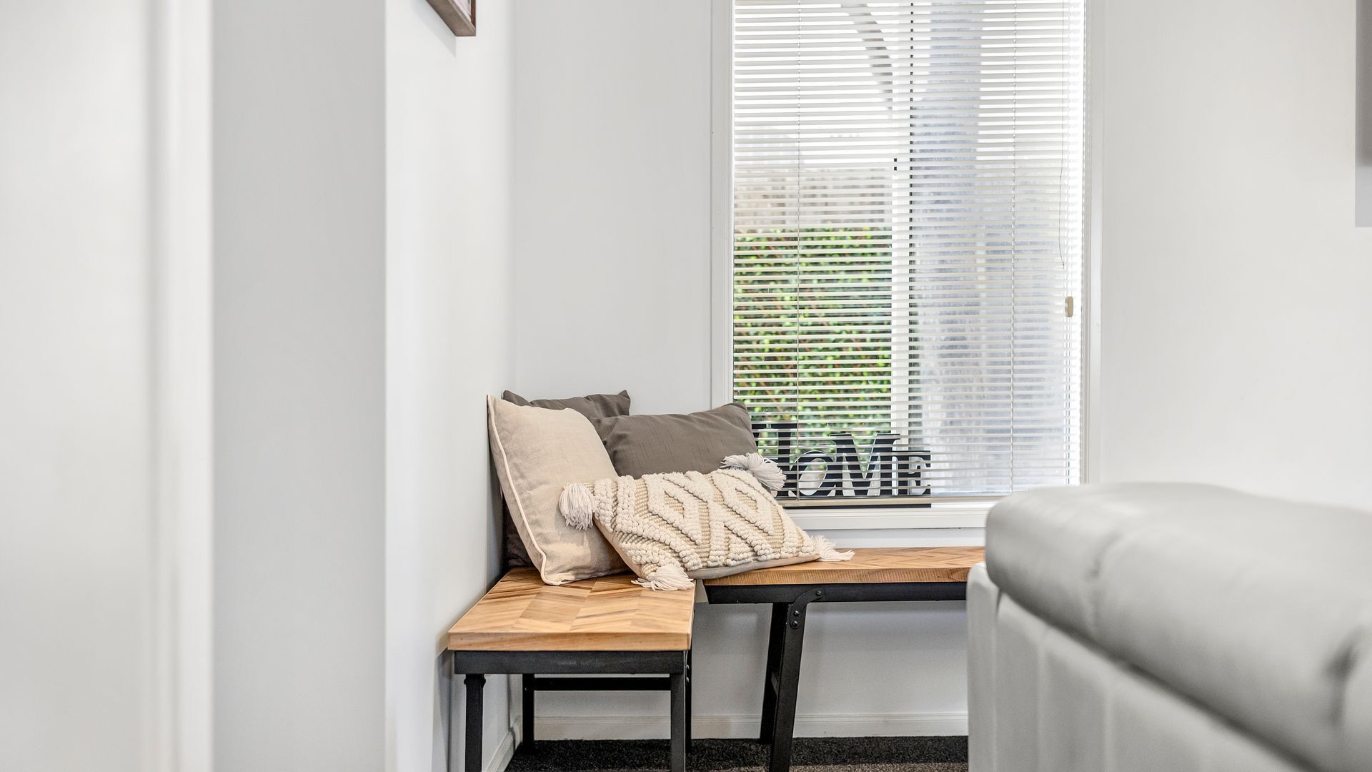 A seating area with a bench, pillows, and a window with blinds.