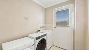 Une buanderie équipée d’un lave-linge et d’un sèche-linge à chargement frontal, d’un petit évier et d’une porte avec une fenêtre.