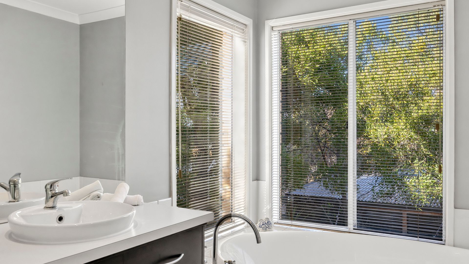 A bathroom with a white sink, a mirror, and a window with blinds.