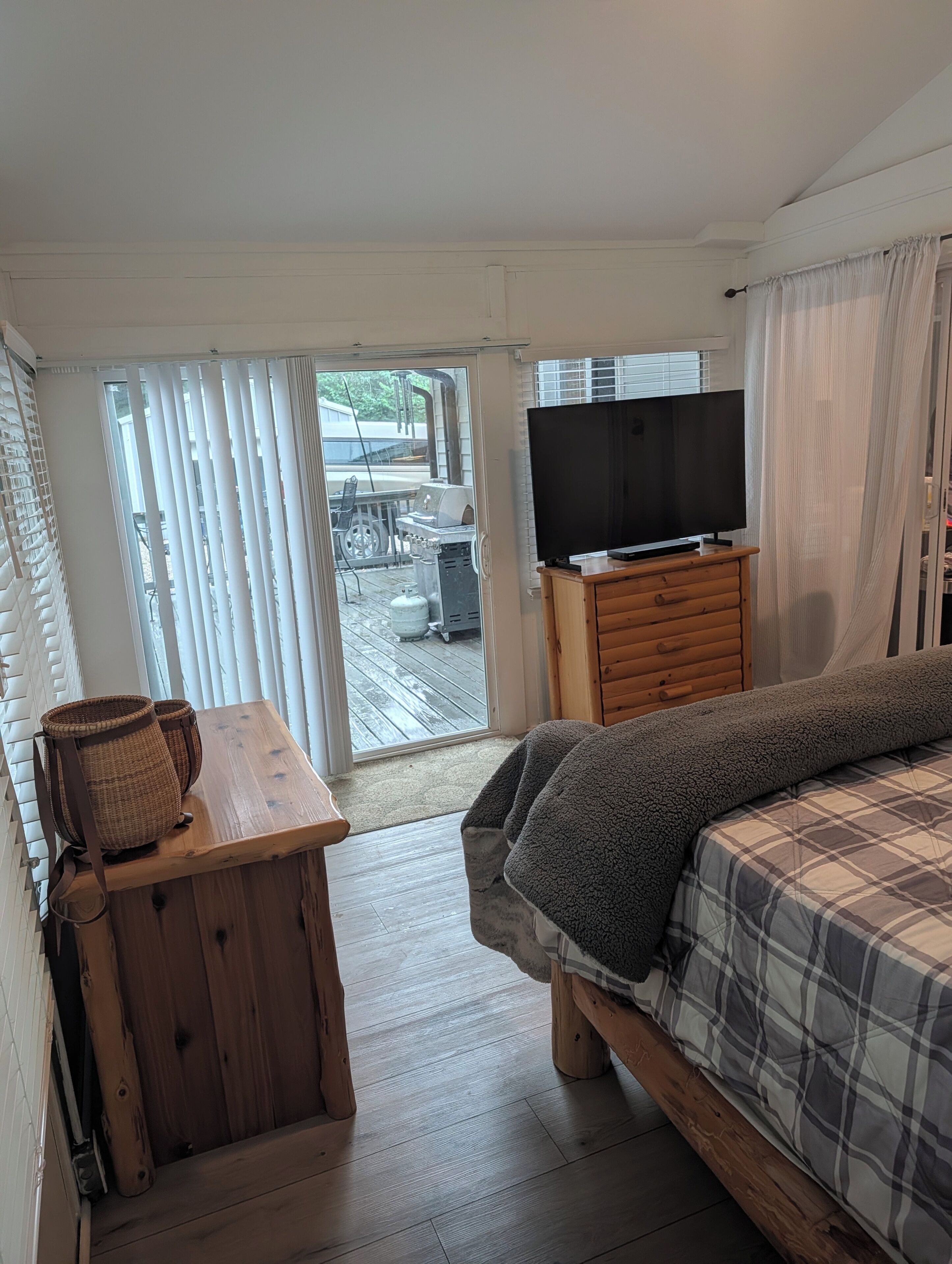 Una camera da letto con un letto, una televisione su un mobiletto in legno, un cesto di vimini e vista sull'esterno attraverso una porta scorrevole.