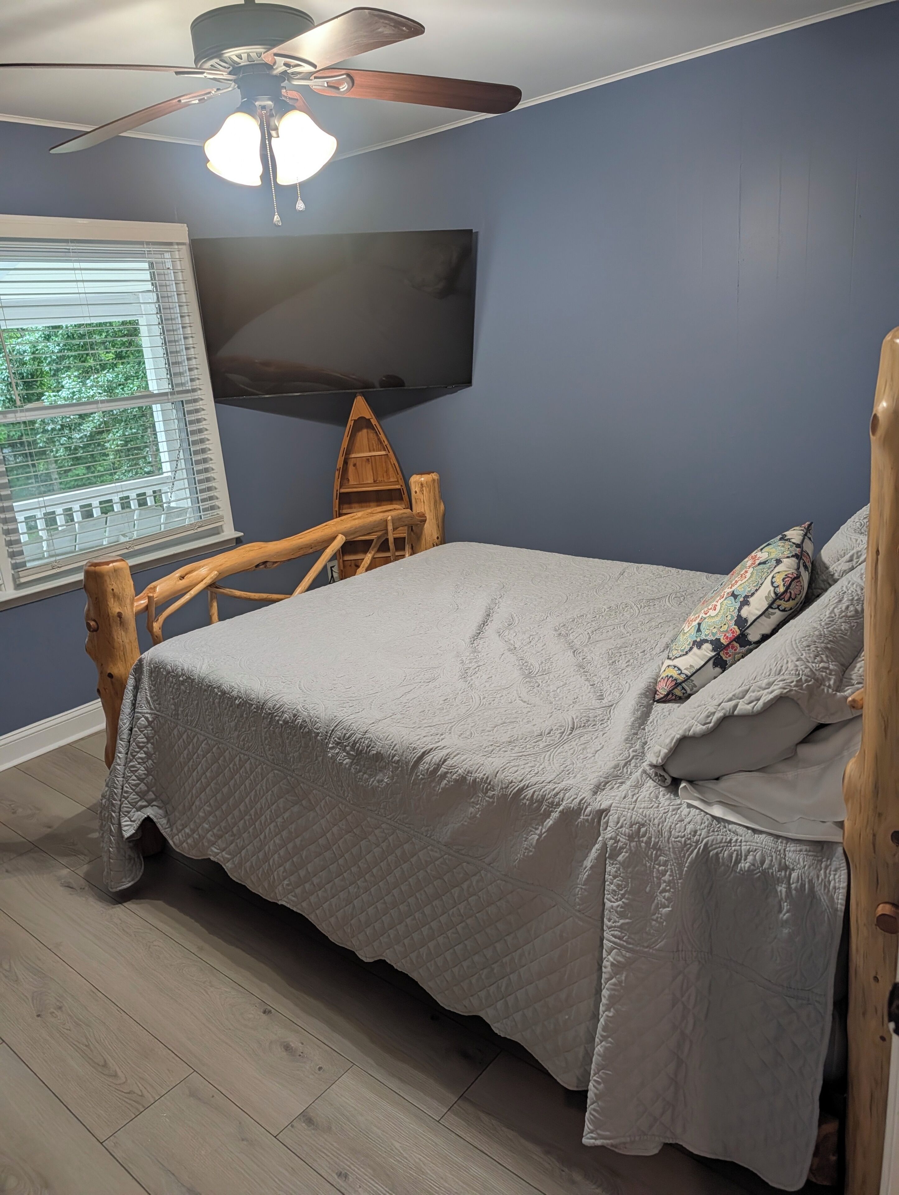 Ein Schlafzimmer mit einem Bett, einem Deckenventilator, einem Fernseher und einem Fenster mit Jalousien.