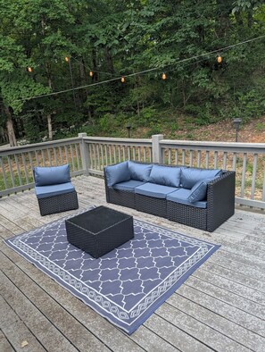 An outdoor deck with a wicker sofa, two matching ottomans, and a patterned rug.