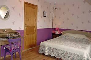 A bedroom with a wooden door, a desk with a chair, a bed with a floral bedspread, and a nightstand with a lamp. - Le Logis du Mesnil B&B: Terraces, Shared Garden, Wi-Fi Included (Saint-Aubin-d'Écrosville)