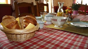 Disposição de café da manhã com uma cesta de vime cheia de croissants, toalha de mesa xadrez e diversos itens para o café.