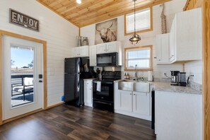 A modern kitchen with white cabinets, a black refrigerator, stainless steel appliances, and a wooden ceiling. - Charming and Modern Tiny Home Escape with Resort Amenities and Pool Near Fredericksburg, TX (Fredericksburg)