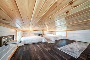 Quarto com duas camas, teto de madeira e chão de madeira escura.