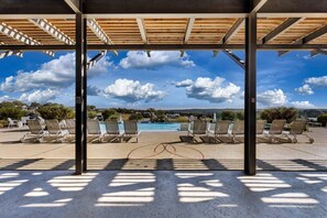 A covered outdoor area with lounge chairs and a pool, under a wooden pergola with a clear sky view. - Charming and Modern Tiny Home Escape with Resort Amenities and Pool Near Fredericksburg, TX (Fredericksburg)