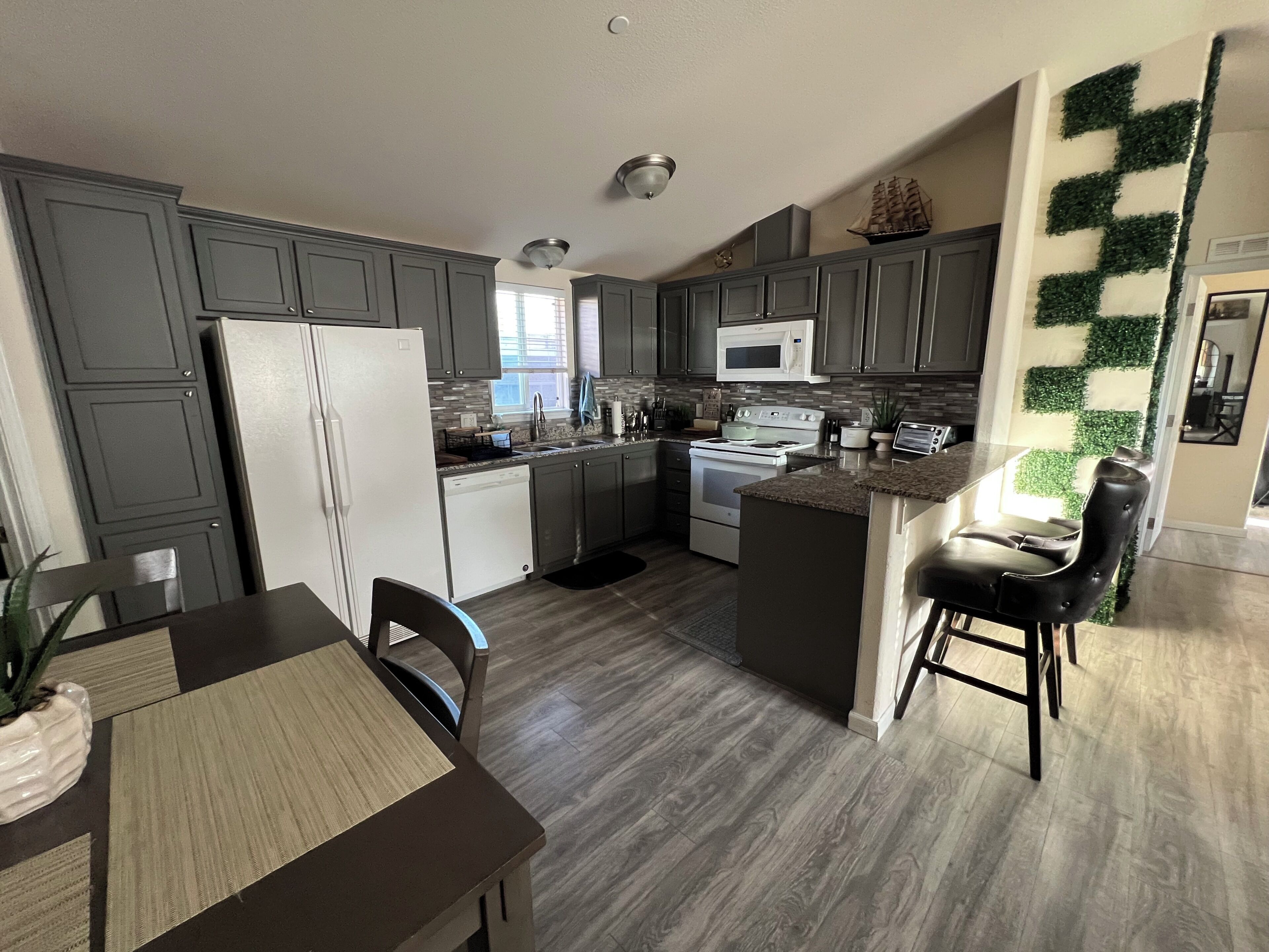 A modern kitchen with grey cabinets, a white refrigerator, a microwave, and a stove. There is a dining area with a table and chairs.