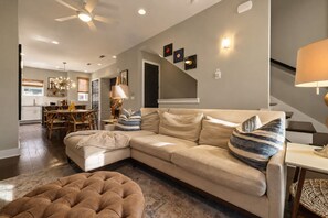A modern living room with a sectional sofa, ottoman, and a dining area with a wooden table and chairs. - NEW! Nashville Era Nights & Rooftop Dreams (Nashville)