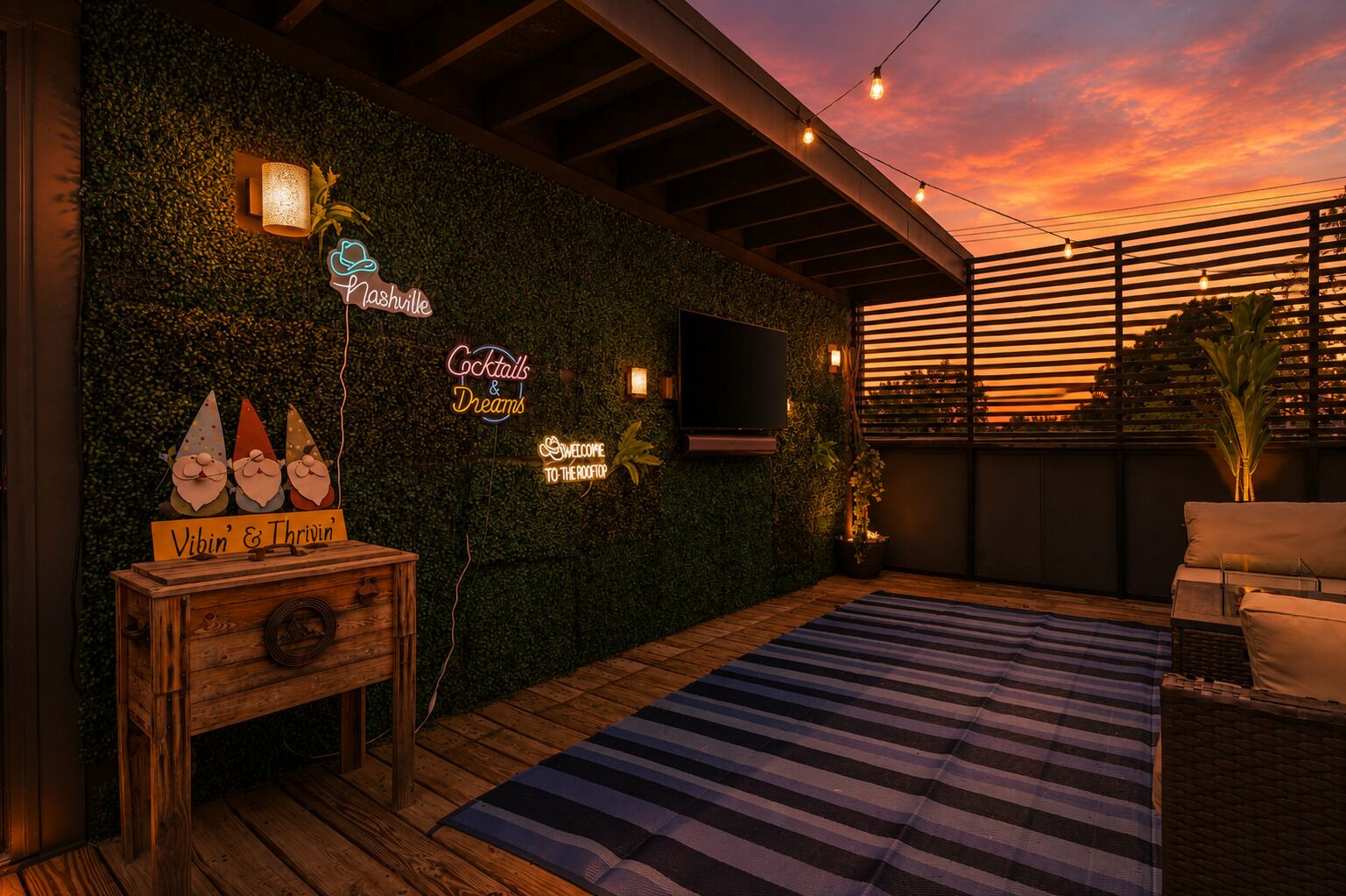 Una terraza en la azotea con un muro verde, luces de neón, una mesa de madera y un tapete a rayas.
