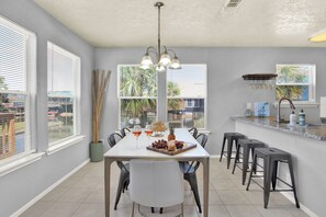 Eine moderne Küche mit Essbereich, ausgestattet mit einem weißen Tisch, Barhocker und Blick ins Freie.