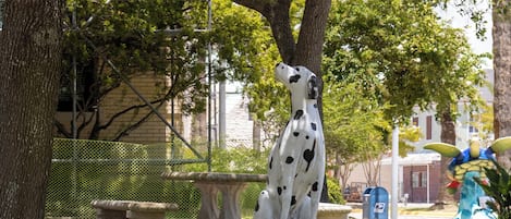Une statue de dalmatien dans un parc, avec un banc, un arbre et une clôture en arrière-plan.