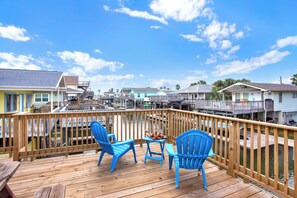 A wooden deck with blue chairs and a table, overlooking a marina with boats and houses. - Canal-Front | Private Boat Slip | Minutes to Beach (Jamaica Beach)