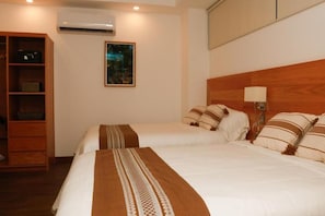 Habitació d'hotel amb dos llits, un panell de capçalera de fusta, una taula de nit, un aire condicionat fixat a la paret i un quadre emmarcat.