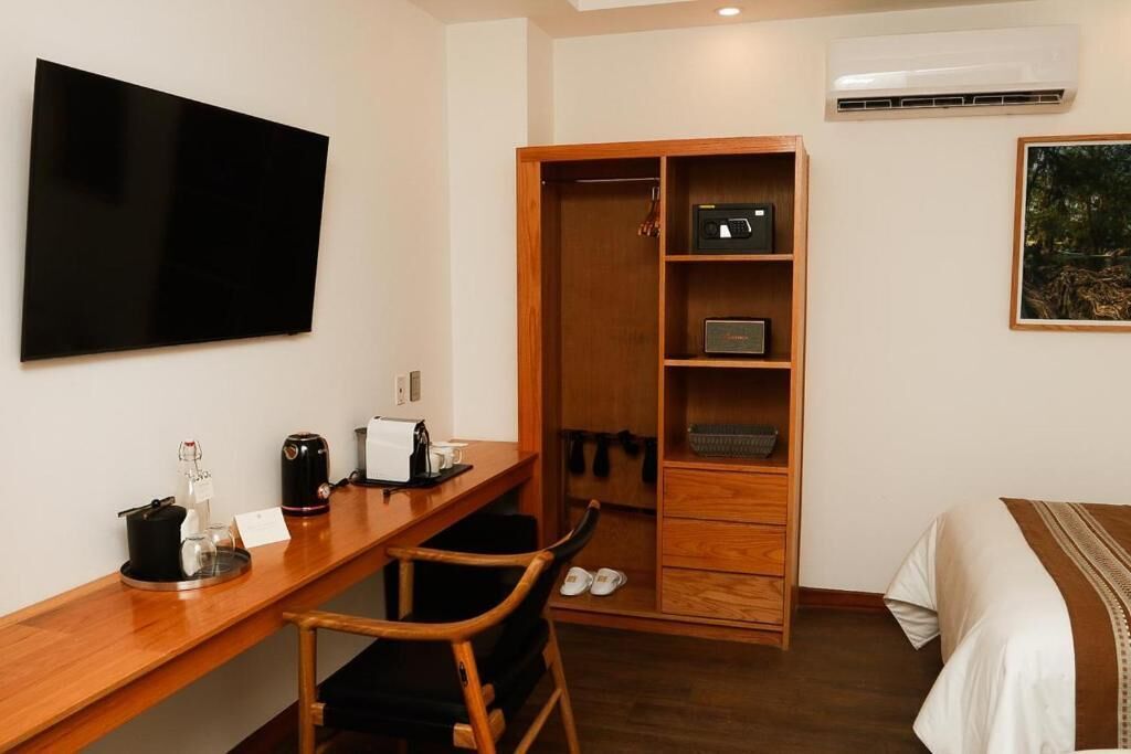 A hotel room with a wooden desk, a television, a wardrobe, and a bed.
