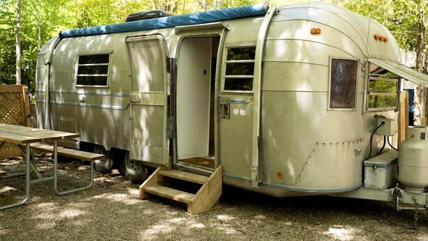 Uma caravana vintage com teto coberto, porta deslizante e um pequeno degrau para a entrada.