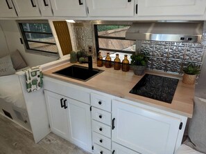 A compact kitchenette with a sink, stove, and storage cabinets. - Glamping in an Airstream: Beautiful Accommodation near Tobermory, Canada (Northern Bruce Peninsula)