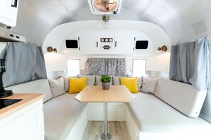 A compact RV interior with a kitchenette, a dining area, and a seating area with cushions. - Glamping in an Airstream: Beautiful Accommodation near Tobermory, Canada (Northern Bruce Peninsula)