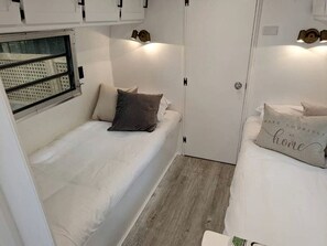 A compact bedroom with a single bed, a window, and a door. - Glamping in an Airstream: Beautiful Accommodation near Tobermory, Canada (Northern Bruce Peninsula)