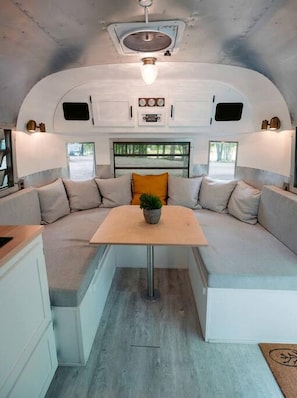 A compact RV interior with a kitchenette, seating area, and a small table with a plant. - Glamping in an Airstream: Beautiful Accommodation near Tobermory, Canada (Northern Bruce Peninsula)