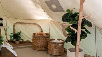 A tent interior with a tripod stand, wicker baskets, and a potted plant.