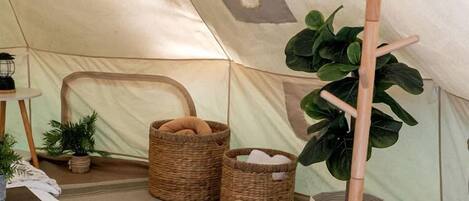 Interior de una carpa con un trípode, cestas de mimbre y una planta en maceta.