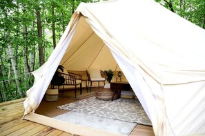 A tent with a table and chairs inside, surrounded by a forest.