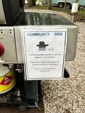 A community BBQ grill with a sign indicating its availability for use by glampers in tents and trailers.