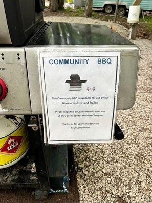 A community BBQ grill with a sign indicating its availability for use by glampers in tents and trailers.