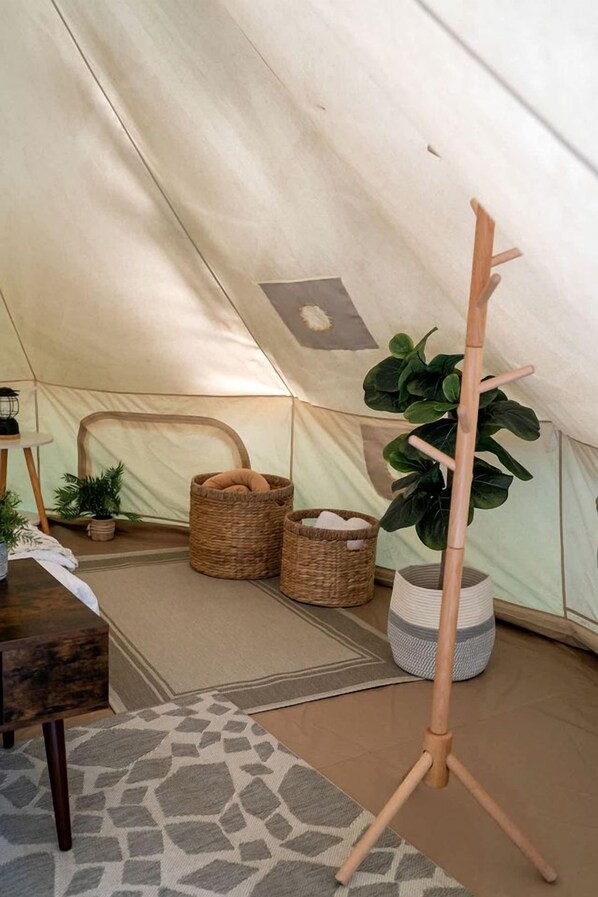 A tent interior with a tripod stand, wicker baskets, and a potted plant.