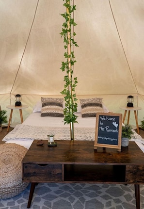 A cozy tent with a bed, a welcome sign, a small table with a candle, and a plant.