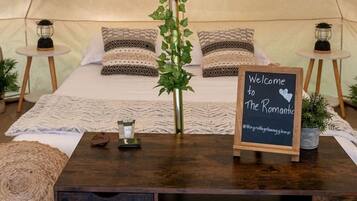 A cozy tent with a bed, a welcome sign, a small table with a candle, and a plant.