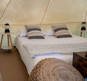 A bed with patterned pillows, a knitted blanket, and a small round rug in a tent-like room with two lantern-style lights on side tables.