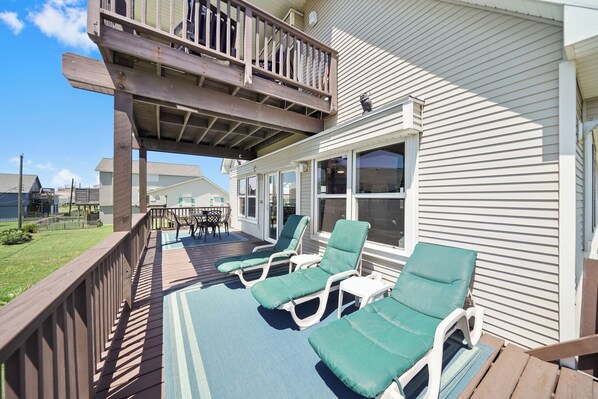 A covered outdoor deck with lounge chairs and a wooden railing.