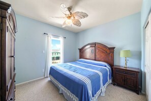 A bedroom with a bed, a ceiling fan, a nightstand, and a view through a window.