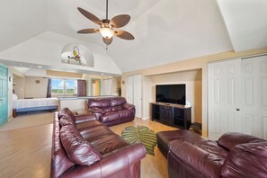A spacious living area with a ceiling fan, leather sofas, a flat-screen TV, and a large window offering a view.