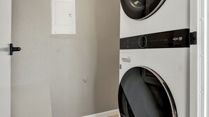 Uma lavanderia com duas máquinas de lavar empilhadas, uma luminária no teto e uma porta com moldura branca.