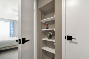 A closet with shelves, a bed, and a window with curtains. - King Bed + Private Garage + Patio | Pool (Galveston)