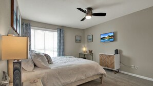 Um quarto com uma cama, um ventilador de teto, uma televisão e uma janela com cortinas.
