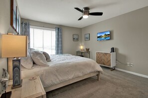 Ein Schlafzimmer mit Bett, Deckenventilator, Fernseher und einem Fenster mit Vorhängen.