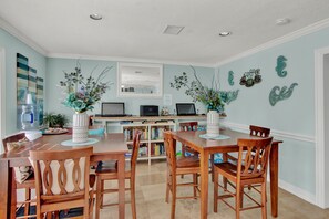 A dining area with a wooden table and chairs, a bookshelf, and decorative wall art. - King Bed + Private Garage + Patio | Pool (Galveston)